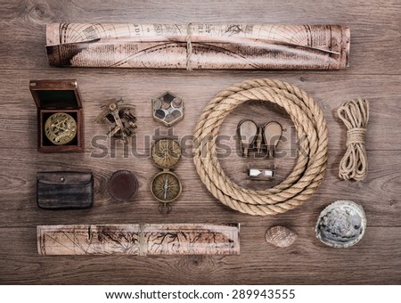 Overhead view of pirate or sailor gear laid out for a backpacking trip on a old wood floor. Items include, rope, compass, money, map, binoculars, hourglass, sextant , shell. Stories background.