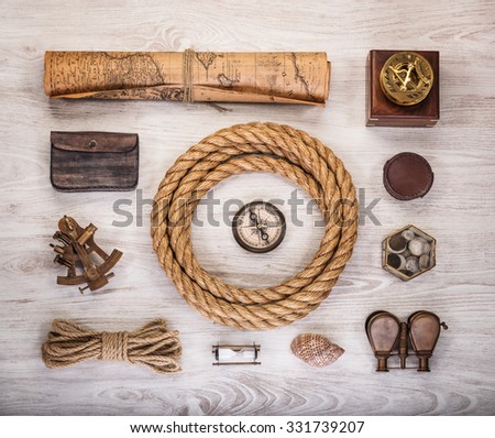 Overhead view of pirate or sailor gear laid out for a backpacking trip on a old wood floor. Items include, rope, compass, money, map, binoculars, sextant , shell. Stories background.