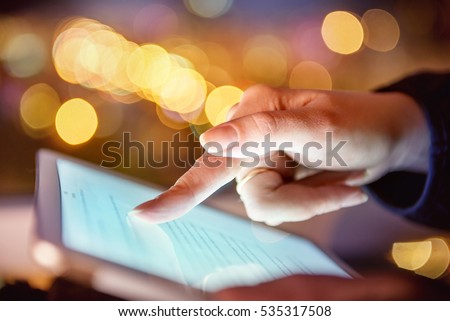 Woman hand hold and touch screen tablet on abstract blurred bokeh of city night light background. Focus in the foreground.