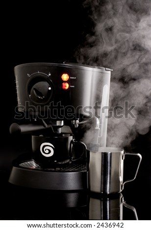 Espresso machine in use with frothing cup and steam against black background