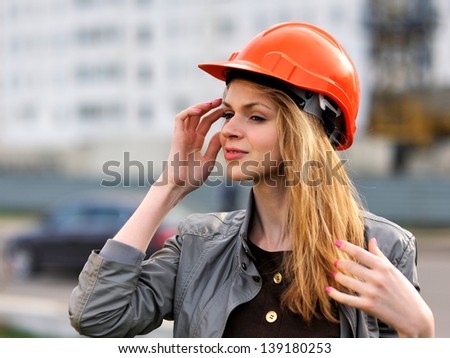 The young pleasant smiling girl with long hair costs against the building under construction