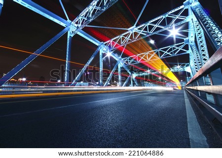 cars run fast across the highway of colorful steel bridge at night