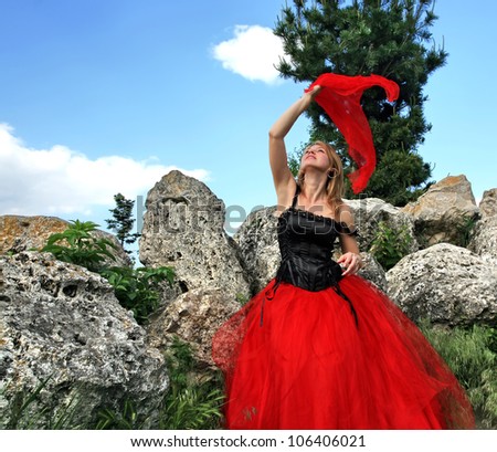 Girl with red scarf and red skirt on the background of rock and sky. Waving a scarf.