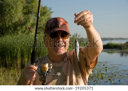 Happy fisherman holding little fish.