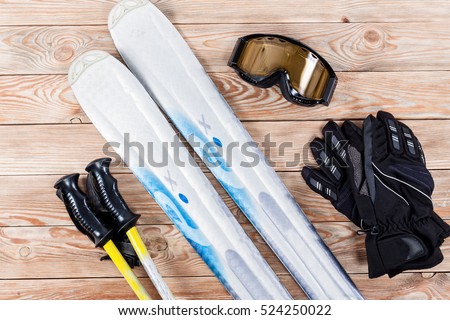 Overhead view of ski accessories placed on rustic wooden table. Items included ski, goggles, gloves and ski sticks. Winter sport leisure time concept.