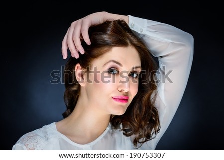 Beautiful young woman with make-up looking smiling confidently, hand over head, studio shot