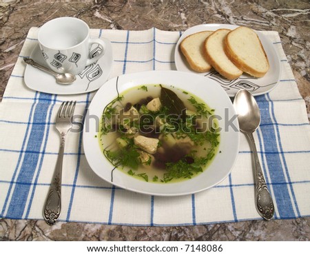 Plate of chicken soup with spoon and bread and tea cup