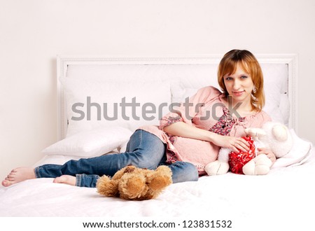 The smiling pregnant young woman on a bed with plush toys