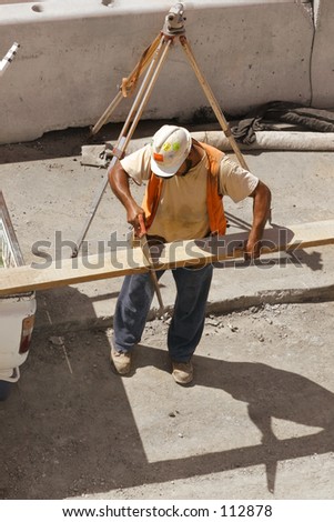 Builder saws a plank of wood.  Builders survey tripod in the background.