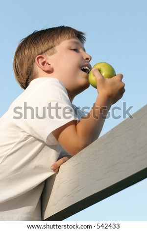 Health & Diet:  Boy on a fence eating  juicy green apple. Health, nutrition, fresh produce