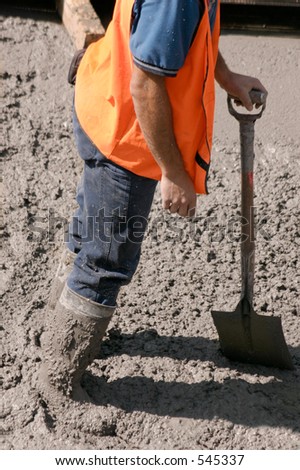 This construction worker stands in wet cement with knee high boots  covered in cement.  He is leaning on his his shovel
