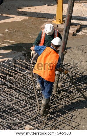 Workers standing on steel mesh pouring concrete through a large hose attached to extendable boom connected to hydraulic truck mounted pump..   There is motion in pouring cement.