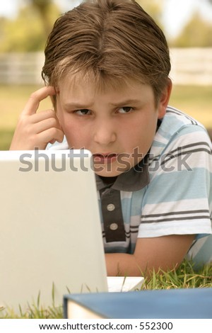 Perplexed:  A puzzled looking boy working on computer outdoors.