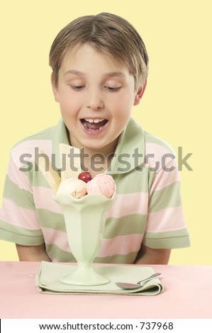 A delighted  boy looks at an ice cream sundae with wafers and cherry on top  placed on a table.
