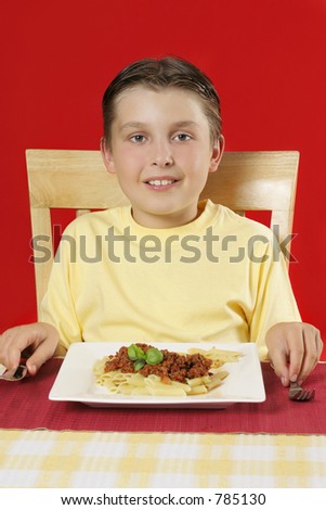 A smiling child at the table with plate of food in front of him.