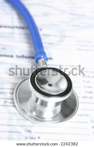 A stethoscope sits on top of a medical record and insurance document.  Medical document has been blurred.