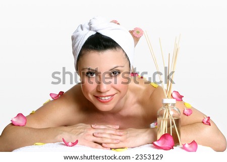 Smiling woman wearing head turban relaxes amongst fragrant rose petals and aroma sticks.