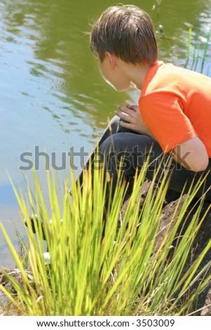 A child sitting at the edge of the lake peering into the water on a beautiful sunny day.