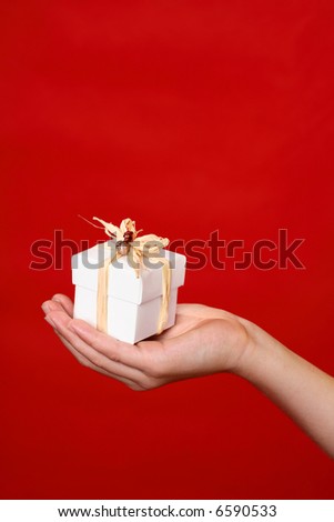 A wrapped and decorated giftbox in the palm of a hand against a red backdrop - suitable for Christmas, birthday or other special occasion