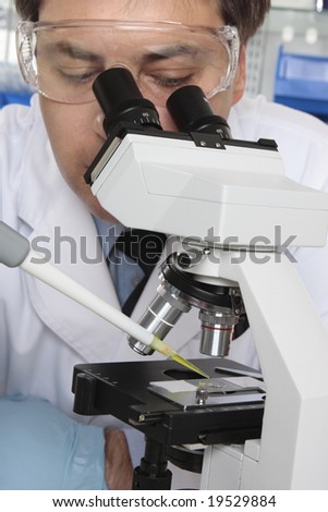 Scientist drops a substance onto a slide  and studies it under the microscope.  Focus to pipette and slide.