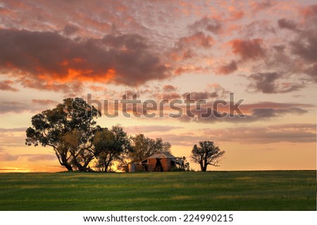 Australian outback sunset.  Old farm house, crumbling walls and verandah w sits abandoned on a hill at sunset. The last sun rays stretching across the landscape painting the grass in dappled light