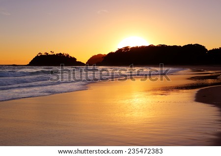 The golden sun rises behind the headland and detached island at Number One Beach, Seal Rocks NSW Australia.  The beach is 1.3km long and curves around to face