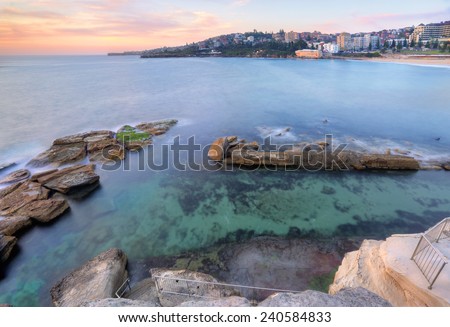 The view from the headland down into Giles Baths rockpool at Coogee in a mid tide.  At low tide the rockshelf at bottom of stairs will become exposed.  Long exposure taken at sunrise.