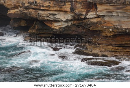 Ocean flows wash in and out of sea caves at the bottom of steep sandstone cliffs