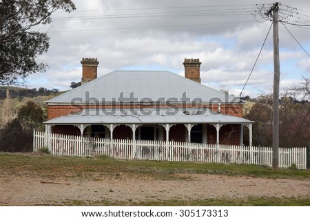 Old run down Australian house with corrugated iron roof, verandah with fancywork and  white picket fence in rural countryside scene.  A bygone era.