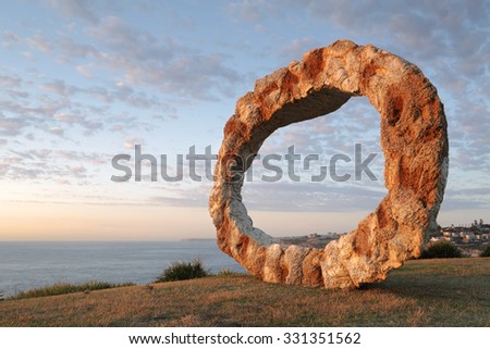 BONDI, AUSTRALIA - OCTOBER 25, 2015;  Annual Sculpture by the Sea free public event.  Exhibit titled Open by Peter Lundberg made of cast concrete with early morning sunlight touching its eastern face