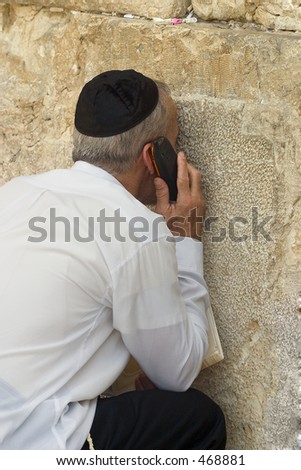 A man speaking on his cellphone while touching the wailing wall.