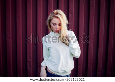 Blonde cute girl fashion look. Photo in the summer park in day light. The wind fluttering hair.