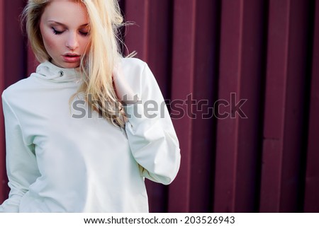 Blonde cute girl fashion look. Photo in the summer park in day light. The wind fluttering hair.