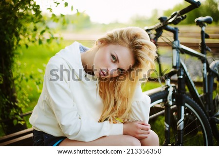 Beautiful girl sitting against bike outdoor in the park looking at you