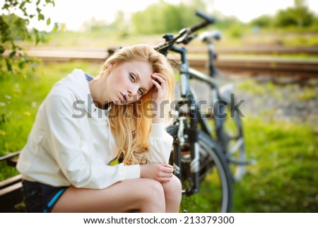 Beautiful girl sitting against bike outdoor in the park looking at you