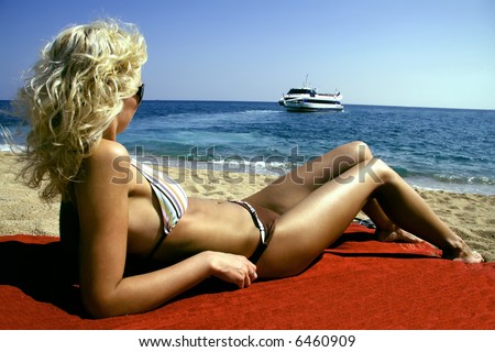 Beautiful young and slender woman model relaxing on beach and watching a ship on sea. Costa Brava beach.