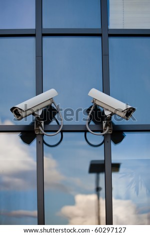 Two security cameras attached on business building with reflections