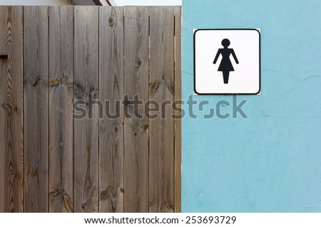 Ladies Toilet Sign on an Exterior Wall next to a Wooden Door