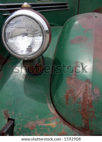 Rusted fender and head lamp on green vintage auto