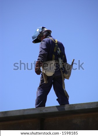 Welder walking along a steel beam at the top of a high rise building project