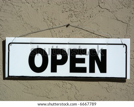 Open sign hanging by a nail on an adobe wall
