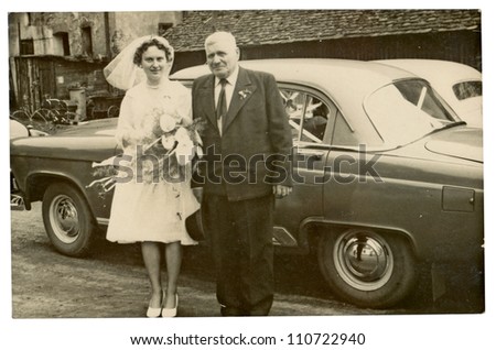 PRAGUE, CZECHOSLOVAKIA, CIRCA 1955 - Bride and her father posing with a car in a farmyard - circa 1955