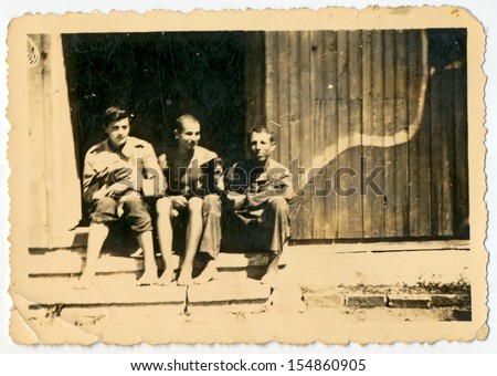 CENTRAL BULGARIA, BULGARIA - CIRCA 1945: Three men sitting on the porch of the house with the puppy in his arms - Note: slight blurriness, better at smaller sizes - circa 1945