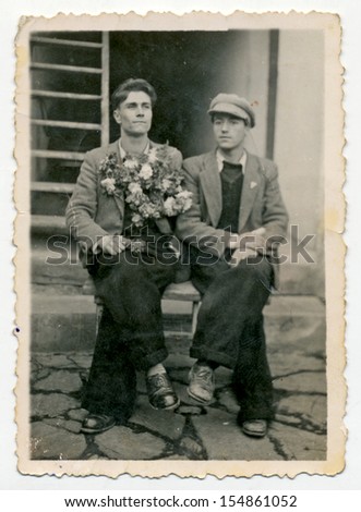 CENTRAL BULGARIA, BULGARIA - CIRCA 1945: Two young men sitting on a bench on the stone porch of the house - Note: slight blurriness, better at smaller sizes - circa 1945