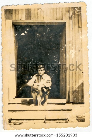 CENTRAL BULGARIA, BULGARIA - CIRCA 1940: Young man sitting on the porch of a country house (with the dog) - Note: slight blurriness, better at smaller sizes - circa 1940