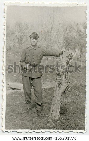 CENTRAL BULGARIA, BULGARIA - CIRCA 1950: Soldier posing in the orchard of trees (or urban park), and relies on the old trunk - Note: slight blurriness, better at smaller sizes - circa 1950