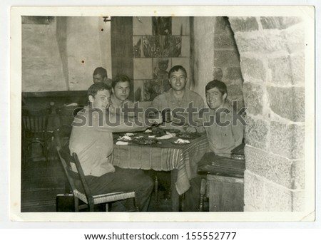 CENTRAL BULGARIA, BULGARIA - CIRCA 1965: Four young soldiers sitting in a village pub and toast to the health of wine - Note: slight blurriness, better at smaller sizes - circa 1965