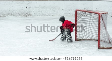 Lone goalie waits in anticipation as the offence gets closer to his net.  Hockey season, kids play the national game at a winter carnival.