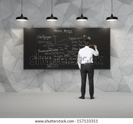 Businessman writing about home sales, standing in front of blackboard with lamps 1