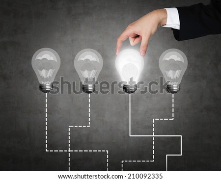 A hand chooses one lightbulb out of four other. A metaphor of the right decision.